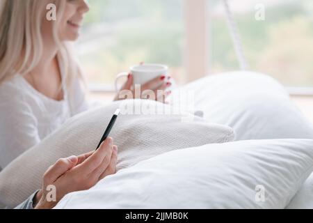 Brautpaar Flitterwochen Planung Bett Tasse Smartphone Stockfoto