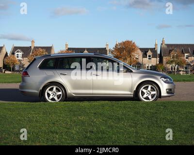 Seitenprofil eines VW Golf Estate an einem Spätherbsttag, geparkt neben grünen Rasenspielfeldern, mit Steinhaus im Hintergrund. Stockfoto