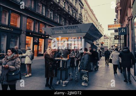 Die Leute vor einer Wurst stehen auf der Straße zwischen schönen alten Gebäuden in Wien, Österreich Stockfoto