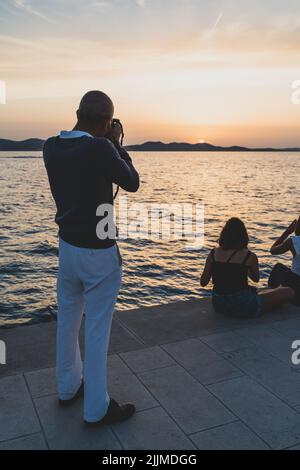 Eine Rückansicht eines Mannes mittleren Alters, der ein Foto eines wunderschönen Sonnenuntergangs in Kroatien gemacht hat Stockfoto