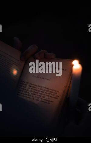 Eine vertikale Aufnahme eines Buches in einer Personenhand unter Kerzenlicht in Medea, Algerien Stockfoto