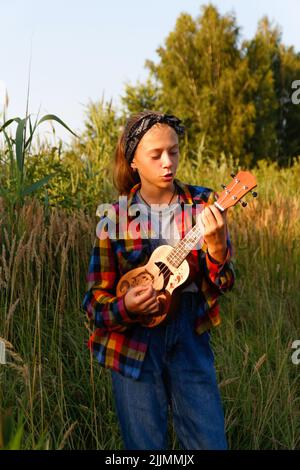 Defokussieren Mädchen mit Gitarre. Teen Mädchen zu Fuß auf Natur Hintergrund. Kleines Mädchen draußen. Grüne Wiese. Generation z. Herbst. Bandana. Lifestyle. Dre Stockfoto