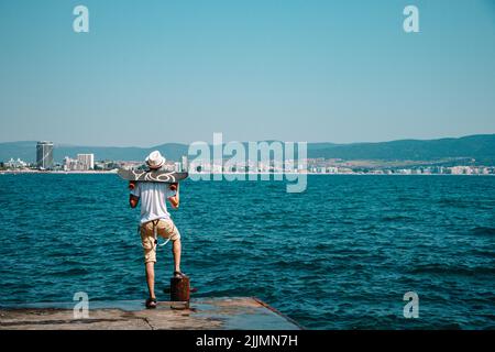 Eine Rückansicht eines Mannes, der auf einem Gehweg steht und ein Skateboard hält Stockfoto