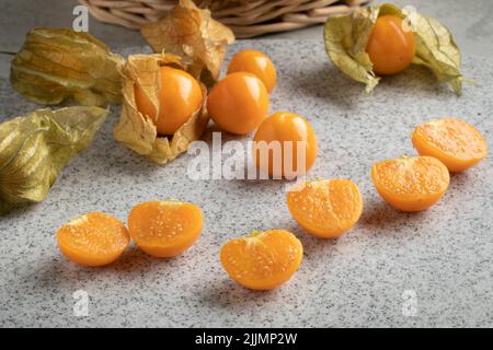 Frische ganze und halbierte Cape Stachelbeere, Physalis peruviana, mit Schale auf Holzhintergrund aus nächster Nähe Stockfoto