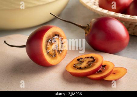 Frische reife geschnittene Tamarillo Nahaufnahme auf einem Schneidebrett und ganze im Hintergrund Stockfoto