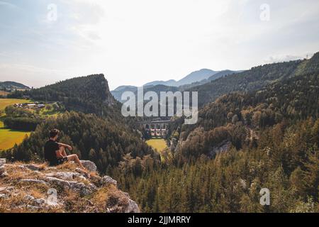 Blick auf einen Touristen und das Bahnviadukt Kalte Rinne und einen vorbeifahrenden Zug im Semming-Gebiet, Rax-Schneeberg-Gruppe in der Steiermark, Österreich. Stockfoto