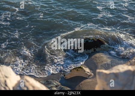 Eine Nahaufnahme der Wellen, die während des Sonnenuntergangs auf den Sandstrand treffen Stockfoto