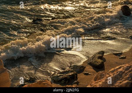 Eine Nahaufnahme der Wellen, die während des Sonnenuntergangs auf den Sandstrand treffen Stockfoto