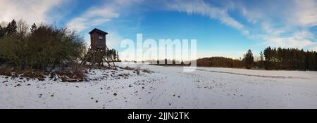Ein Luftpanorama des schneebedeckten Feldes mit Jagdturm im Hintergrund von Bäumen Stockfoto