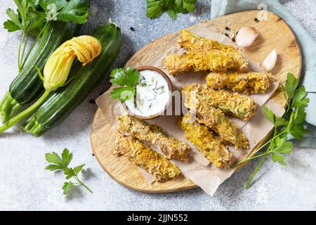 Gesunde, leckere Snacks, sommerliches Essen. Zucchini-Pommes. Knusprige Zucchini-Sticks in Paniermehl, mit Käse mit Knoblauch-Joghurt-Sause. Blick von oben. Stockfoto