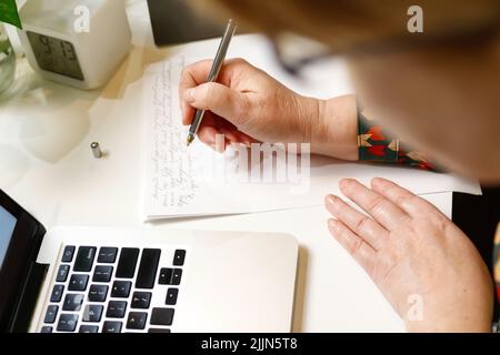 Defokussieren weiblicher Hand Schreibfeder. Unkenntlich elegante Frau, die im Büro am Computer arbeitet. Beginn oder Ende eines Arbeitstages. Arbeitsbereich. Draufsicht. Zeit Stockfoto