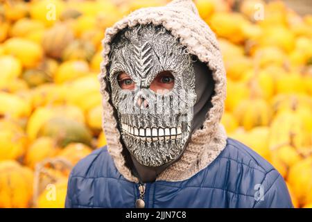 Unschärfe Halloween Menschen Porträt. Person in grimmiger Reaper Maske auf gelbem Kürbis Hintergrund stehend. Halloween-Horror. Schädelgeist. Grimmiger Schnitter. Hallo Stockfoto