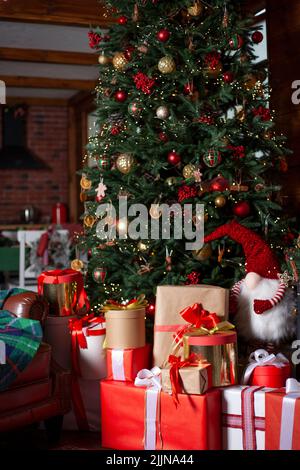 Weihnachtsbaum mit Lichtern und Geschenken. Geschenk in roter Verpackung. Startseite gemütlicher Urlaub. Die Atmosphäre des neuen Jahres. Weihnachten Hintergrund. Stockfoto