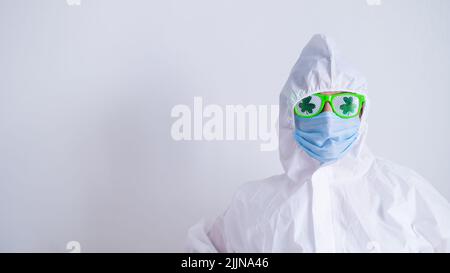 Eine Frau in einem Schutzanzug und einer medizinischen Maske und mit einer lustigen Brille feiert den St. patrick's Day Stockfoto
