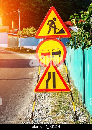 Gelb-rote Warnschilder auf der Schotterseite einer Landstraße. Straßenarbeiten im Gange Stockfoto