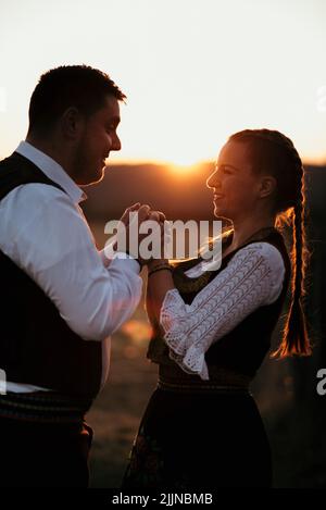 Eine Nahaufnahme eines jungen serbischen Paares in traditioneller Tracht auf dem Feld Stockfoto