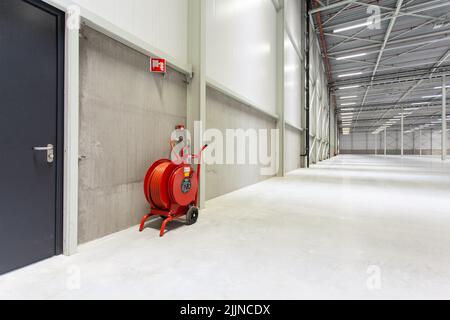 Ein roter Löschschlauch in einem neuen leeren Lagerhaus Stockfoto