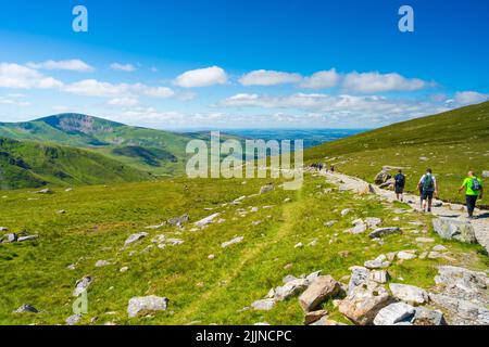 SNOWDON, WALES - 09. JULI 2022: Wanderer gehen vom Mount Snowdon aus nach dem Erreichen des Gipfels in der Morgendämmerung. Snowdon ist der höchste Berg in Wales, Stockfoto