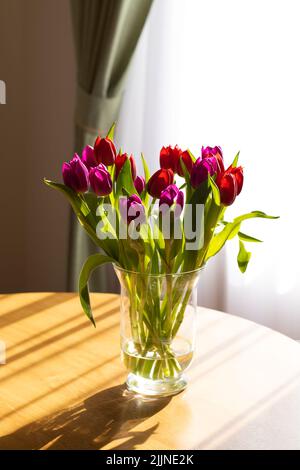 Glasvase auf dem Tisch mit Tulpen, Licht aus dem Fenster und Schatten. Stockfoto