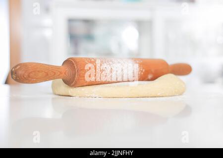 Nahaufnahme eines mit Mehl überzogenen Holzrollbolzens auf frischem Teig auf einer Küchenarbeitsplattfläche Stockfoto