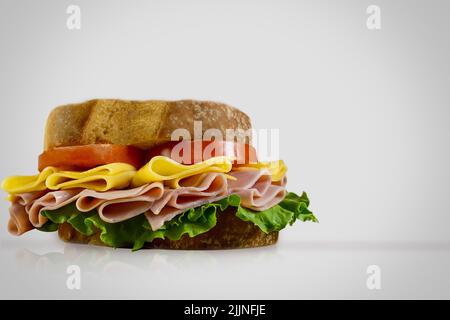 Ein leckeres Schinken-Käse-Sandwich mit frischem Salat und Tomaten auf weißem Hintergrund Stockfoto
