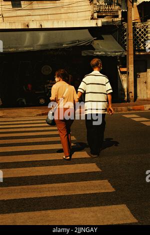 Eine Vertikale eines älteren Paares, das sich beim Überqueren der Straße in Bangkok City die Hände hielt Stockfoto