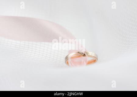 Eine Nahaufnahme eines Eherings mit rosa Band auf der weißen Textur Stockfoto