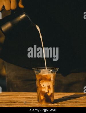 Eine Vertikale, in der ein Barista Milch in eine mit Kaffee gefüllte Plastikbecher gießt Stockfoto