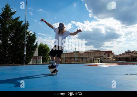 Ein junger blonder Kerl, der Skateboarding-Tricks vorführt und im Skatepark springt Stockfoto