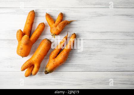 Mehrere reife orange hässliche Karotten liegen auf einer hellen Holzoberfläche Stockfoto