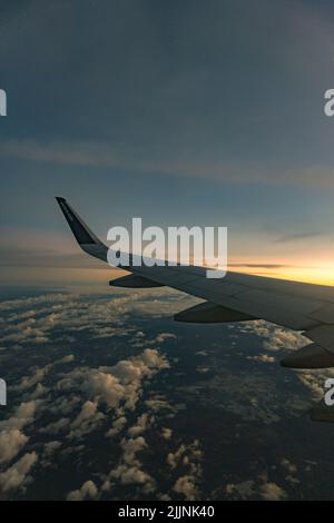 Eine Luftaufnahme vom Flugzeug, der Flügel des Flugzeugs bei Sonnenuntergang von der rechten Seite über dem Wolken-Horizont Stockfoto