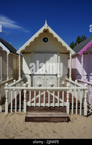 Das Bild zeigt eine Reihe von hellen Strandhütten, die einen Sandstrand säumen und in verschiedenen Farben, einschließlich Rot, Blau und Gelb, gestrichen sind. Stockfoto