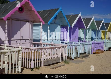 Das Bild zeigt eine Reihe von hellen Strandhütten, die einen Sandstrand säumen und in verschiedenen Farben, einschließlich Rot, Blau und Gelb, gestrichen sind. Stockfoto