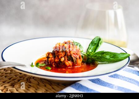 Schüssel mit Fleischbällchen in Tomatensauce mit einem Glas Weißwein Stockfoto