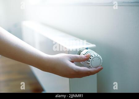 Frau Hand reguliert die Temperatur auf dem Heizkörper, hohe Strom- und Gaspreise, Wirtschaftskrise Stockfoto