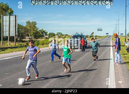 Eine Gruppe von jungen Kindern, die an einem sonnigen Tag in Rosario, Argentinien, Fußball auf der Straße spielen Stockfoto