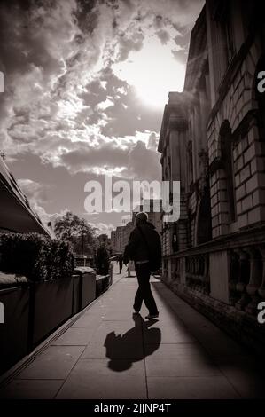 Eine vertikale Aufnahme eines Mannes, der unter einem wolkigen Himmel mit strahlender Sonne auf der Straße läuft Stockfoto