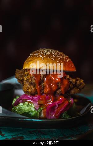 Eine vertikale Aufnahme eines Chicken Burgers in einem dunklen, grungigen Restaurant Stockfoto