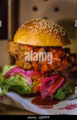 Eine vertikale Aufnahme eines Chicken Burgers in einem dunklen, grungigen Restaurant Stockfoto