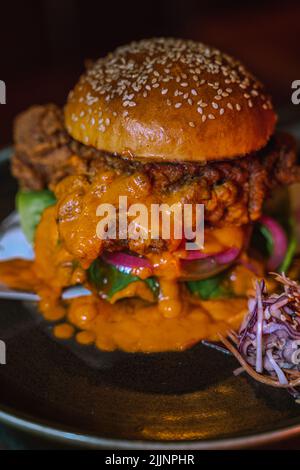 Eine vertikale Aufnahme eines Chicken Burgers in einem dunklen, grungigen Restaurant Stockfoto