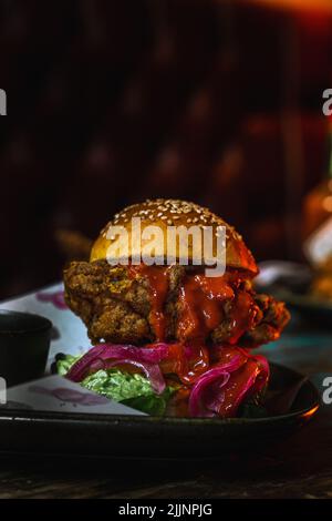 Eine vertikale Aufnahme eines Chicken Burgers in einem dunklen, grungigen Restaurant Stockfoto