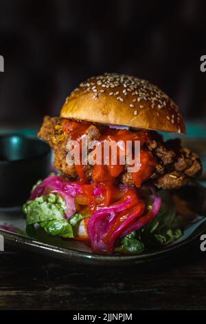 Eine vertikale Aufnahme eines Chicken Burgers in einem dunklen, grungigen Restaurant Stockfoto