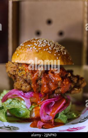 Eine vertikale Aufnahme eines Chicken Burgers in einem dunklen, grungigen Restaurant Stockfoto