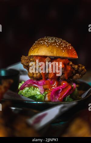 Eine vertikale Aufnahme eines Chicken Burgers in einem dunklen, grungigen Restaurant Stockfoto