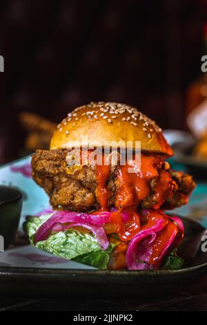 Eine vertikale Aufnahme eines Chicken Burgers in einem dunklen, grungigen Restaurant Stockfoto