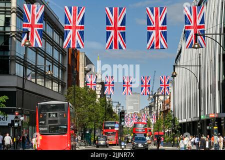 London, England - 2022. Juni: Über der Oxford Street hängen Reihen von Union Jack-Flaggen, rote Londoner Busse fahren entlang der Straße Stockfoto