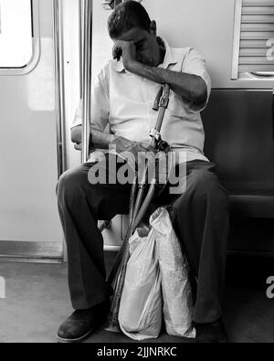 Eine vertikale Graustufenaufnahme eines alten Mannes, der in einer U-Bahn mit einem auftauchenden Stock sitzt Stockfoto