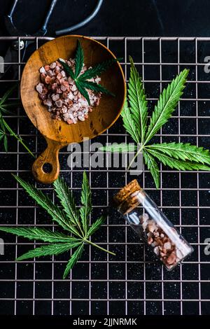Ansicht von oben auf Marihuanablätter und rosa Himalaya-Salz in Glasgefäßen auf einem Metall kühlenden Felsen Stockfoto