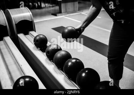 Eine Nahaufnahme in Graustufen von einem Mann, der eine Bowlingkugel in der Hand hält, um sie zu werfen und zu spielen Stockfoto