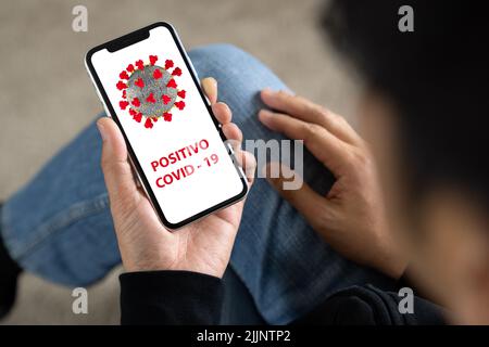 Ein Mann hält einen weißen Bildschirm eines Smartphones von oben und liest Informationen über Covid-19 Stockfoto